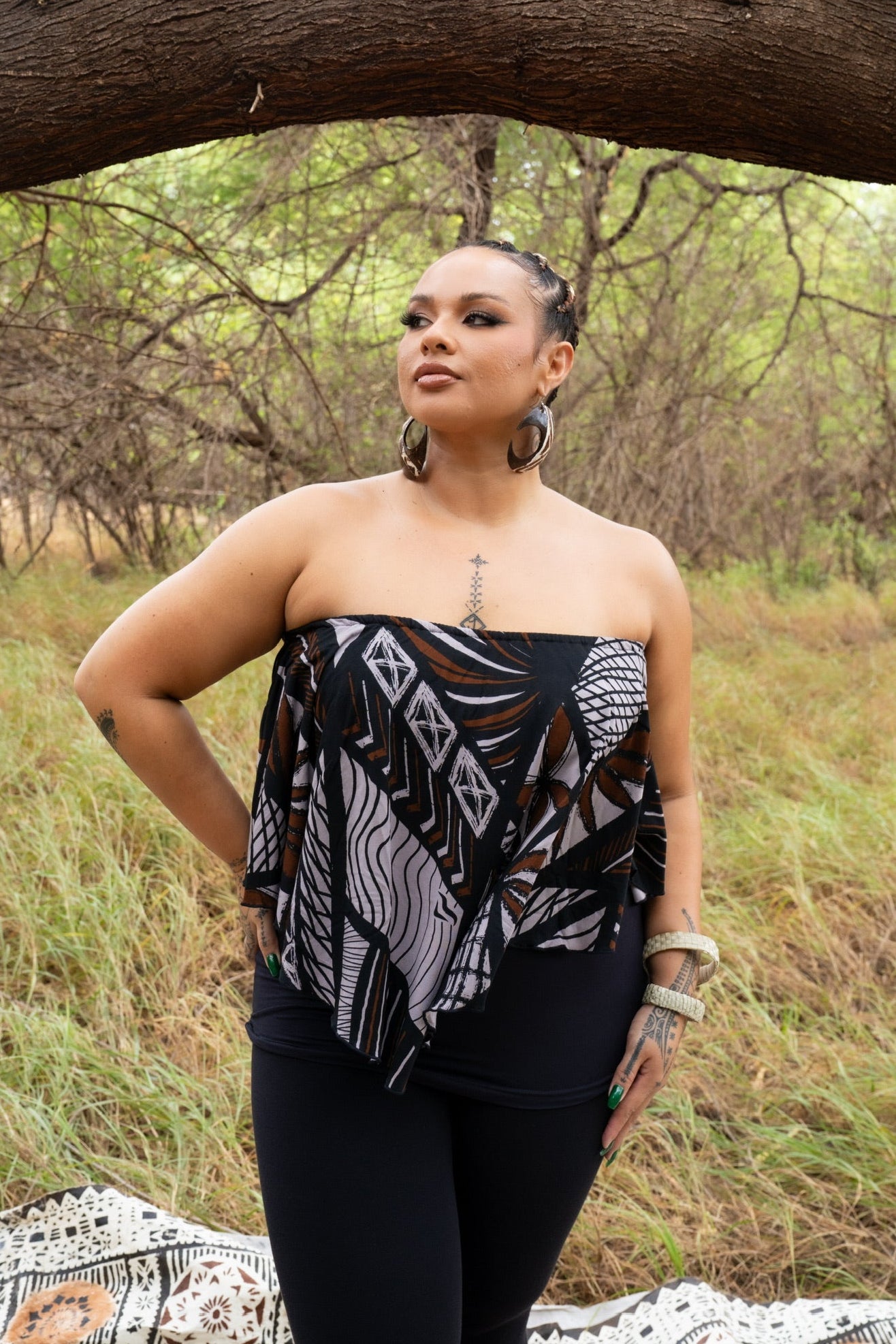 Woman in a strapless black and white patterned top standing under a tree in a natural setting