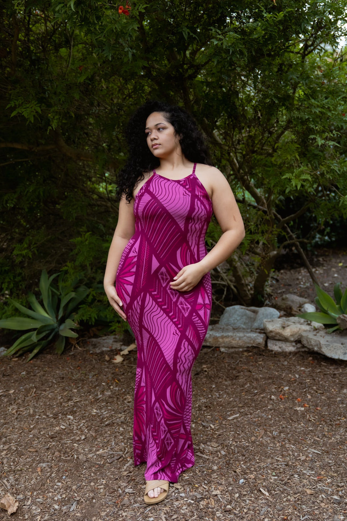 Woman in a pink dress standing in a natural setting with trees and rocks.